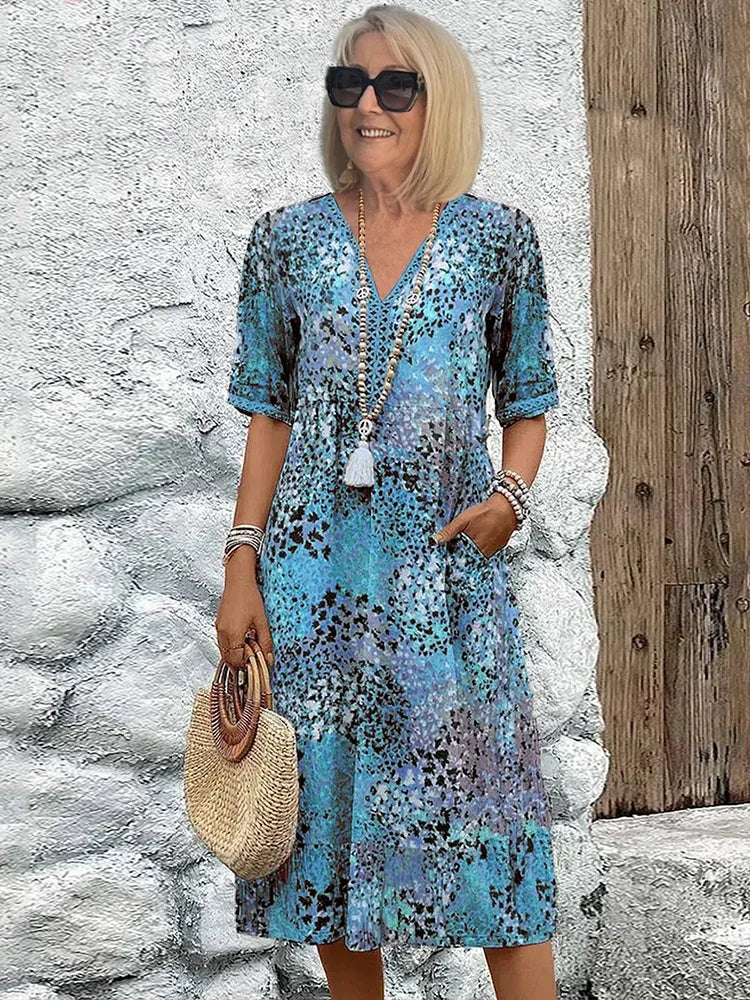Blue tonal animal print midi dress with V-neck and lace-trimmed sleeves styled against a stone wall