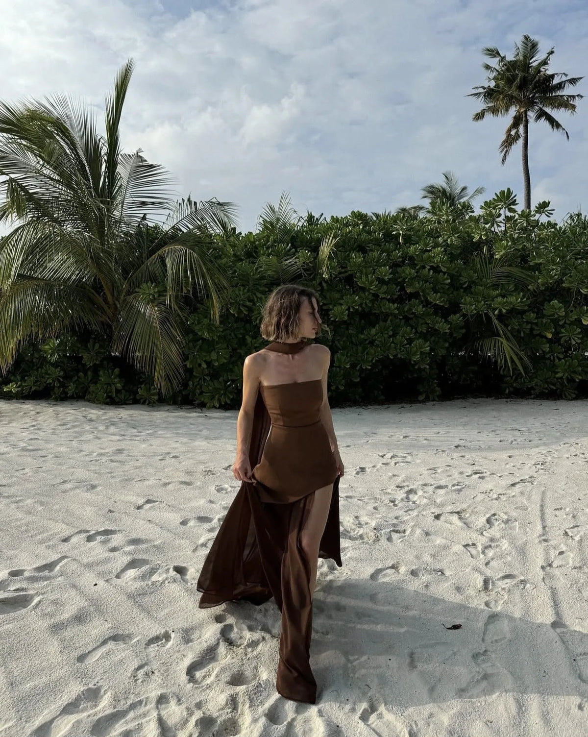 Side angle of white strapless maxi dress showing the asymmetric hemline where the structured top layer meets the sheer chiffon skirt