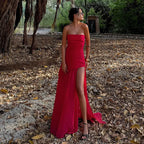 Detail shot of the fitted strapless bodice and asymmetric drape of the white maxi dress against a stone wall backdrop