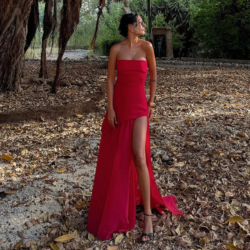 Detail shot of the fitted strapless bodice and asymmetric drape of the white maxi dress against a stone wall backdrop
