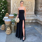 Evening shot of woman in white strapless maxi dress with satin neck tie, seated with one leg exposed through the side slit