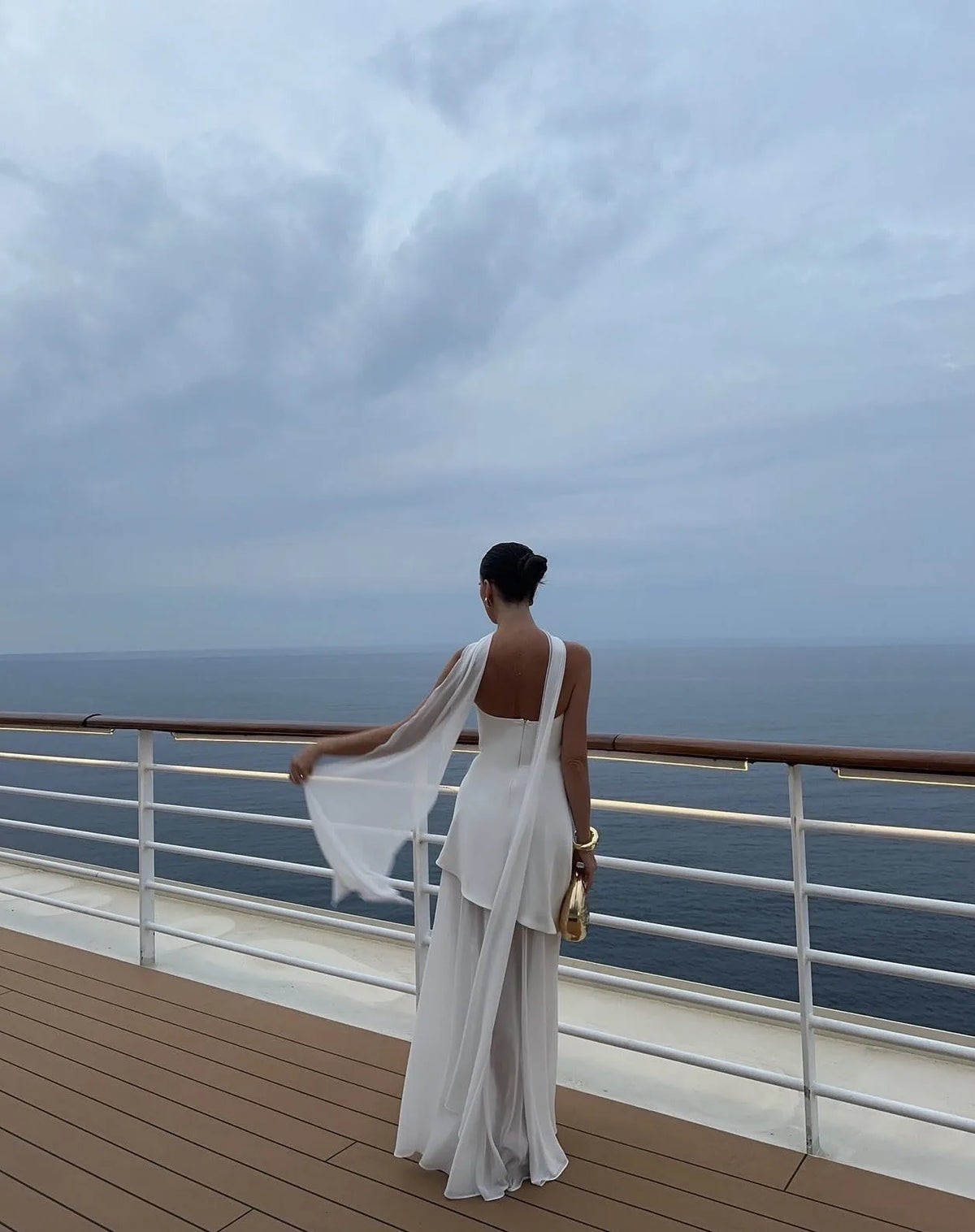Back view of white one-shoulder draped gown showing the flowing chiffon neck tie trailing over the shoulder and open back