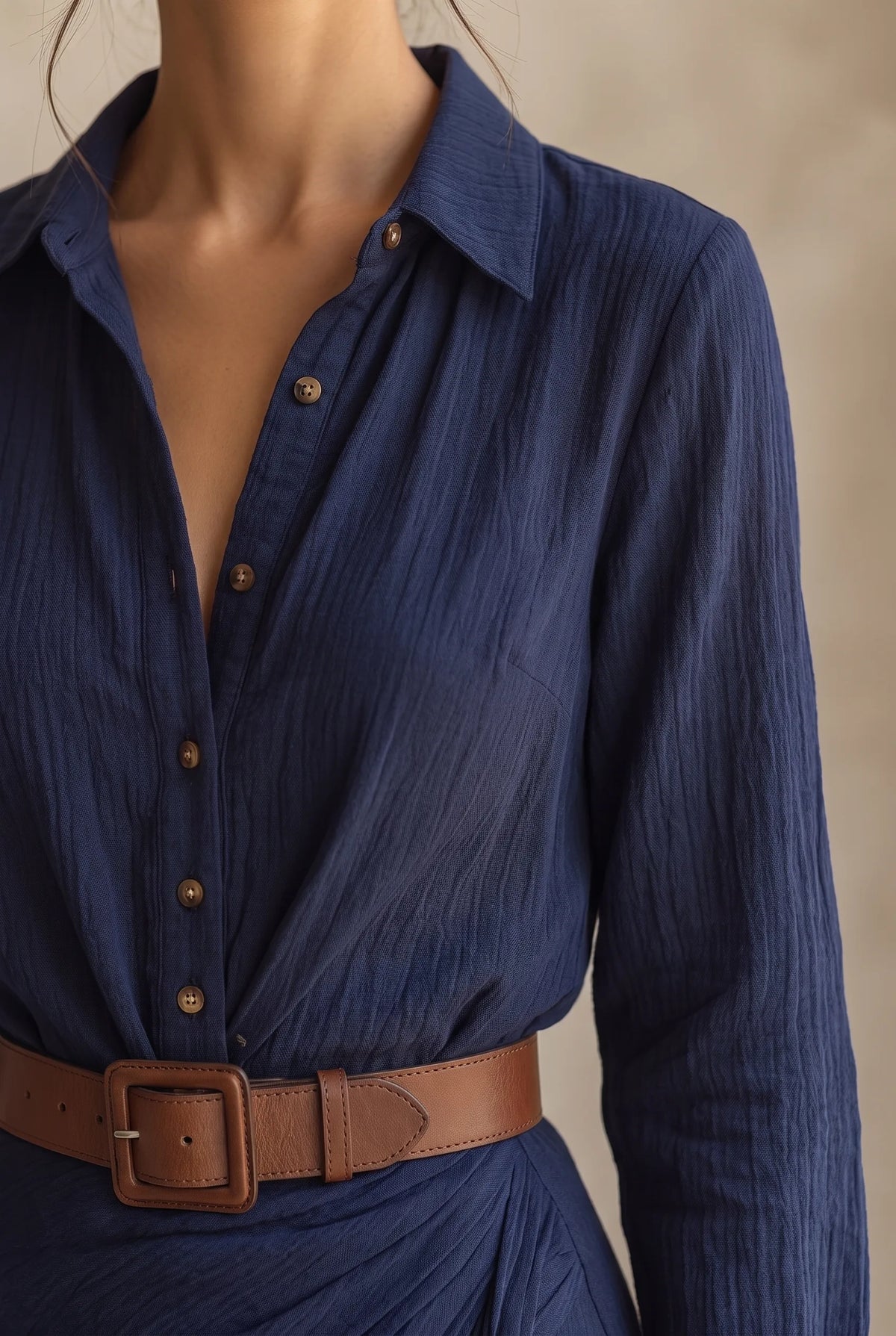 Close-up of the navy dress neckline, button placket and brown leather belt against the textured fabric
