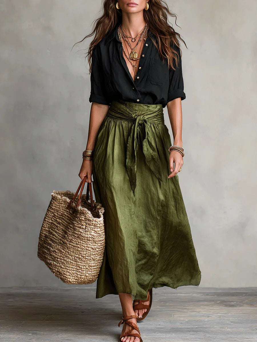 Woman modelling a black button-up long-sleeve shirt with an olive green tie-waist maxi skirt and woven tote bag