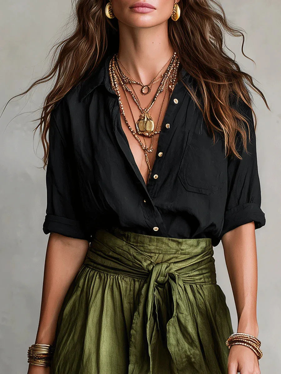 Close-up of the black shirt's collar and button placket layered with gold necklaces