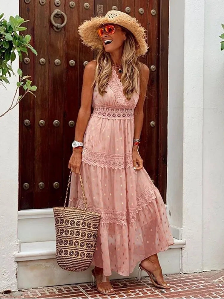 Blush pink tiered maxi dress with lace inserts and shimmering dot print, shown against a rustic wooden door backdrop.
