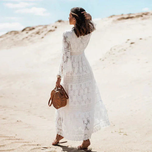 Back view of white lace maxi dress showing flowing silhouette, woven circle bag and strappy sandals on the beach