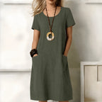 Front view of a model wearing a green short-sleeve linen-look midi dress with a scoop neckline and side pockets