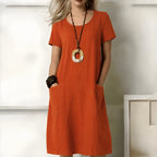 Model wearing an orange short-sleeve relaxed-fit midi dress with a round neckline and functional front pockets