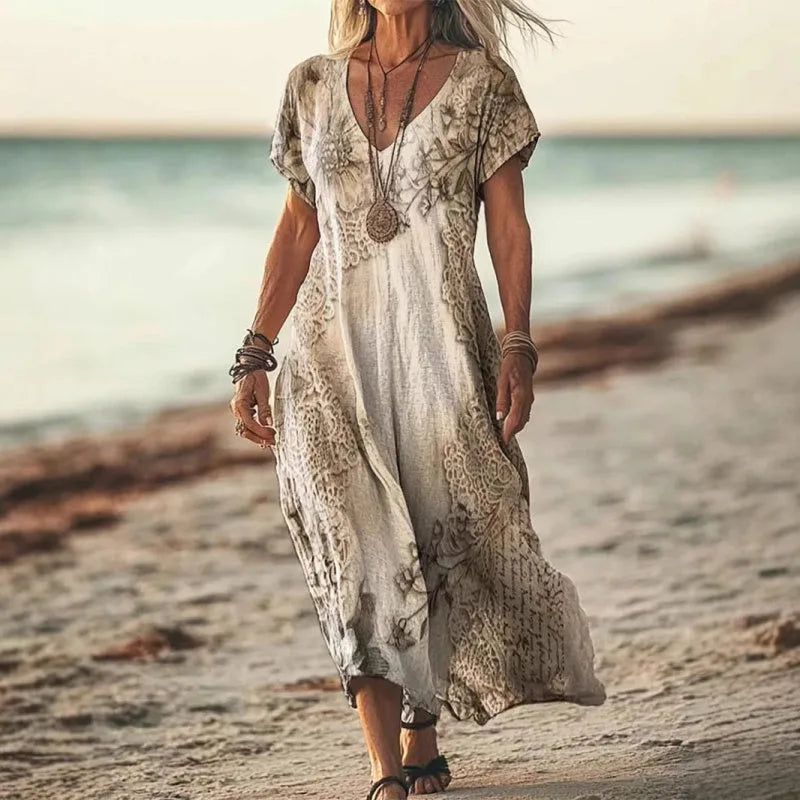Woman walking along the beach wearing the beige floral print maxi dress with layered necklaces