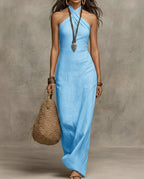 Sky blue linen halter maxi dress with crossover neckline, styled with layered bracelets and a straw tote
