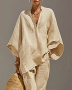 Close-up of a model in a beige textured linen two-piece set with a deep V-neck top and batwing sleeves, paired with a woven tote bag.