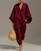 Full-length view of a model walking in a burgundy two-piece set with contrast stitching, batwing sleeve top and tapered jogger-style pants.