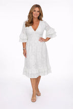 Front view of a woman in a white broderie anglaise midi dress with a deep V-neckline and ruffled bell sleeves