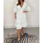 White broderie anglaise midi dress shown on a model against a brick wall, highlighting the fitted smocked waist