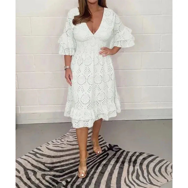 White broderie anglaise midi dress shown on a model against a brick wall, highlighting the fitted smocked waist