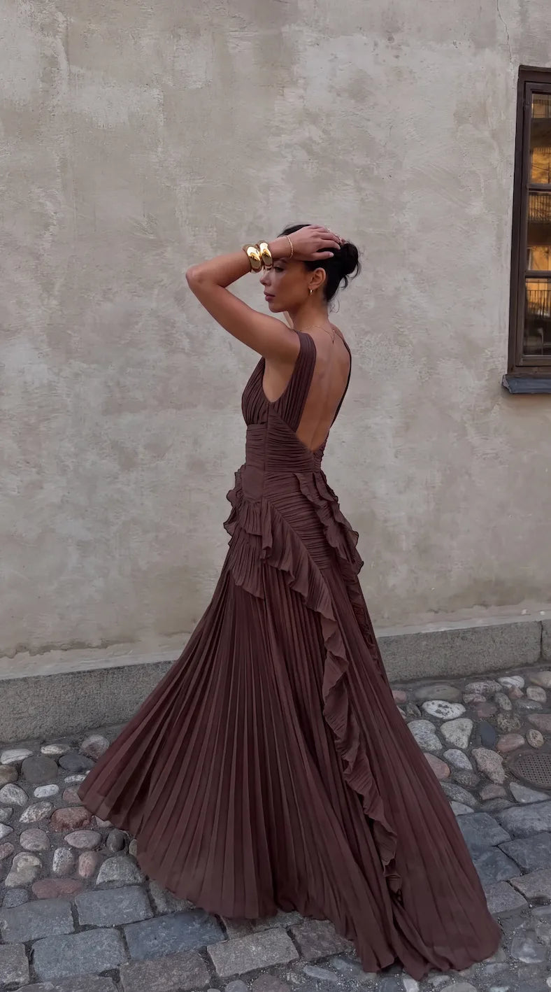 Side profile showing the dress's low back design and flowing pleated skirt train on cobblestone pavement