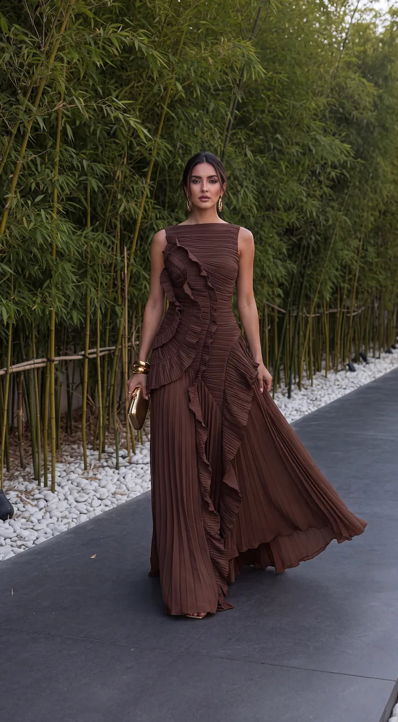 Model walking in the dress with a thigh-high front split and flared pleated hem beside a bamboo hedge