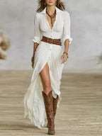 Three-quarter front view of white button-down maxi dress with rolled sleeves, deep neckline and belted waist paired with cowboy boots