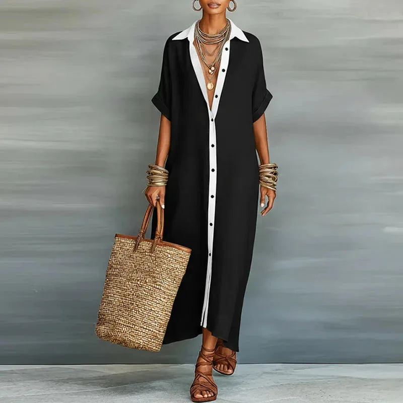 Model wearing a black maxi shirt dress with contrast white placket and collar, holding a straw tote bag