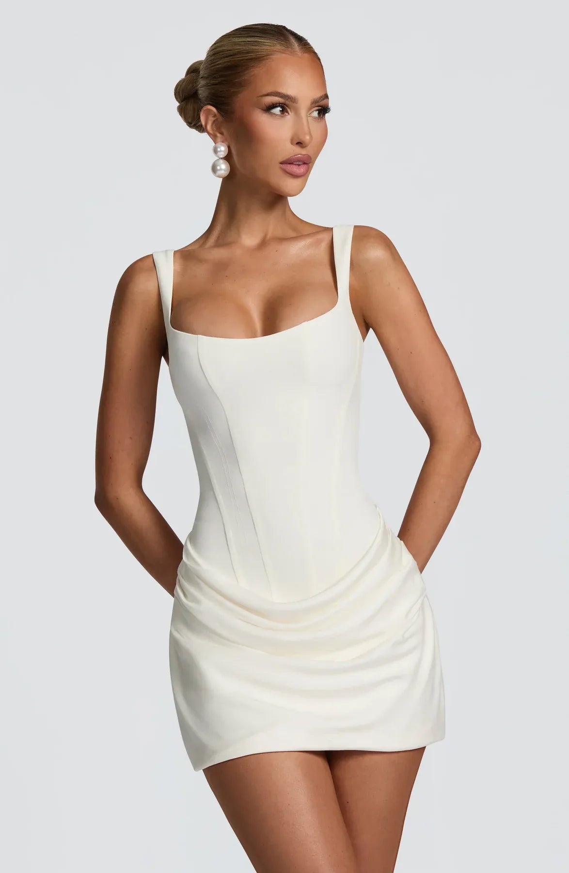 Front view of model wearing an ivory corset-style mini dress with square neckline and draped ruched skirt