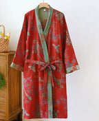 Red floral kimono robe with sage green trim and waist tie, draped on a wooden hanger against a white wall