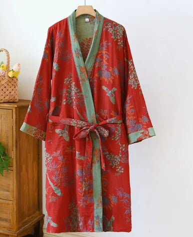 Red floral kimono robe with sage green trim and waist tie, draped on a wooden hanger against a white wall