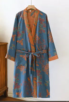 Teal blue kimono robe with an orange botanical bird and branch print, shown hanging near a wooden cabinet