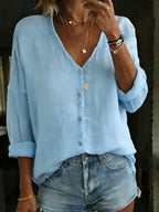 Light blue cotton linen blouse showing loose weave texture, button placket and rolled-up cuffs.