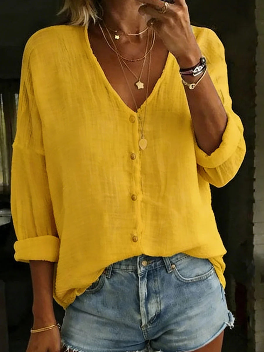 Mustard yellow cotton linen blouse with V-neck button front, styled with layered necklaces and denim shorts.