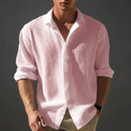Pale pink textured shirt worn open at the collar, showing the relaxed drape and rolled-up sleeve cuffs