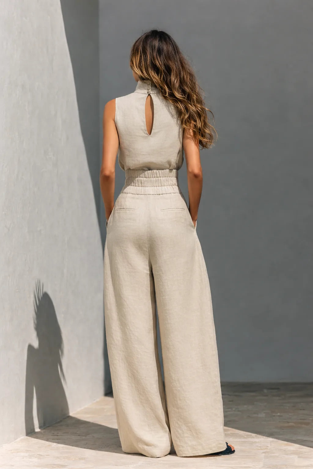 Back view showing the high neck with button keyhole closure and elastic waistband on the beige linen wide-leg pants set