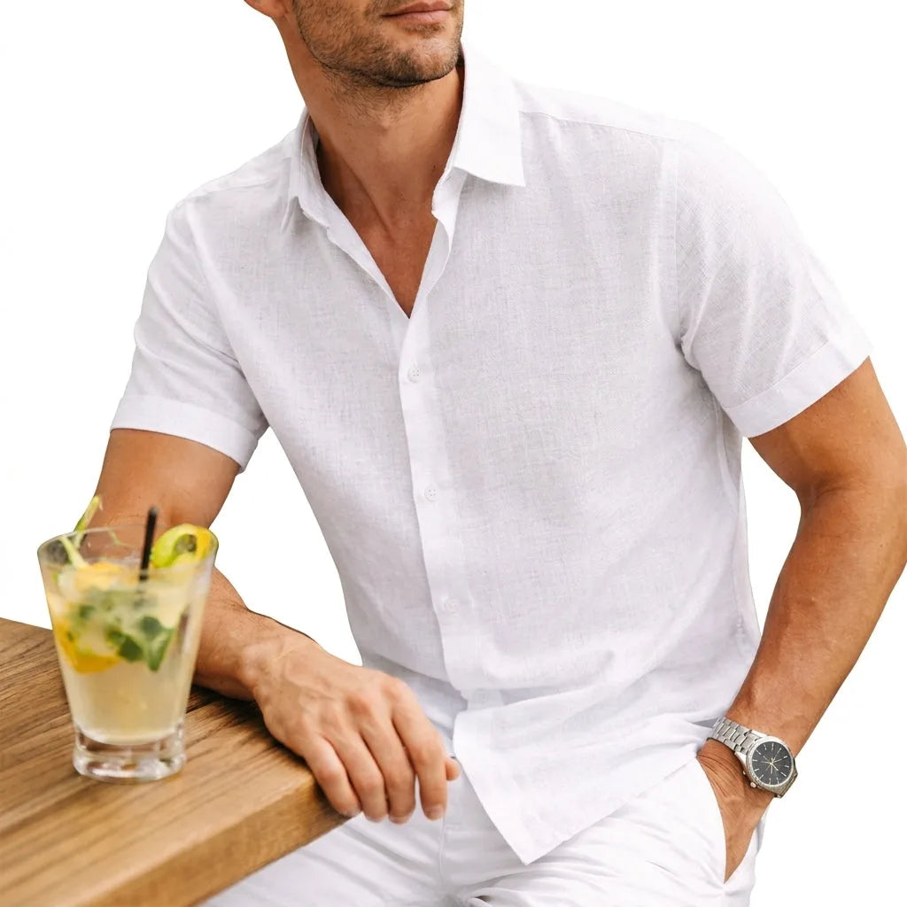 White short-sleeve cotton shirt worn open-necked, paired with white trousers at an outdoor table