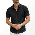 Charcoal black woven shirt with short sleeves, buttoned to the collar, hands clasped at the front