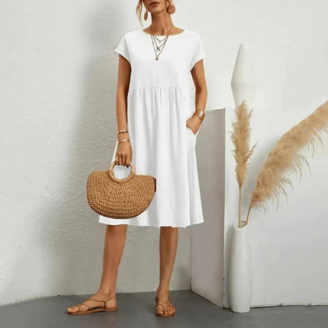 Woman wearing a flowing white short-sleeve midi dress with a tiered swing skirt, holding a woven straw handbag
