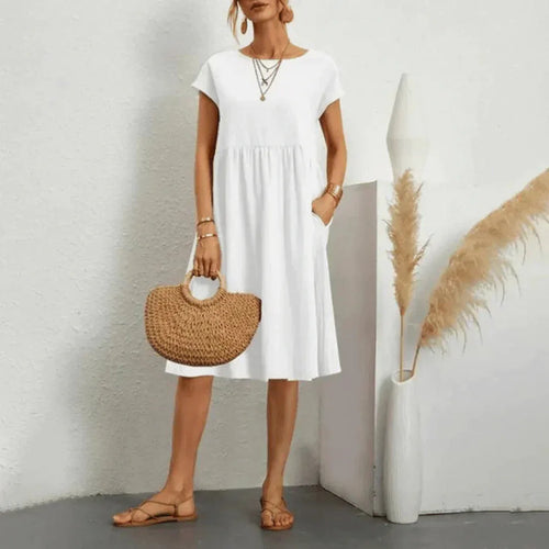 Woman wearing a flowing white short-sleeve midi dress with a tiered swing skirt, holding a woven straw handbag
