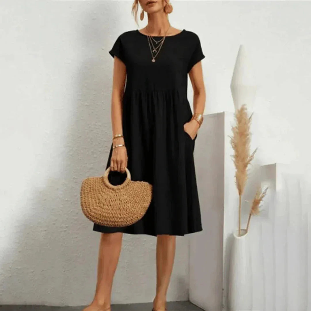 Black tiered swing dress with side pockets, shown against a plain wall with dried pampas grass decor