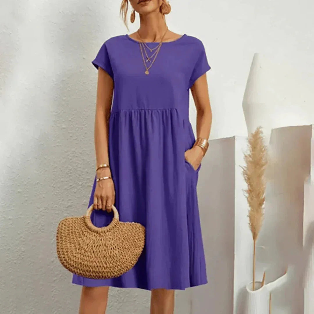 Purple short-sleeve midi dress with a cinched empire waist and flared skirt, paired with a straw tote