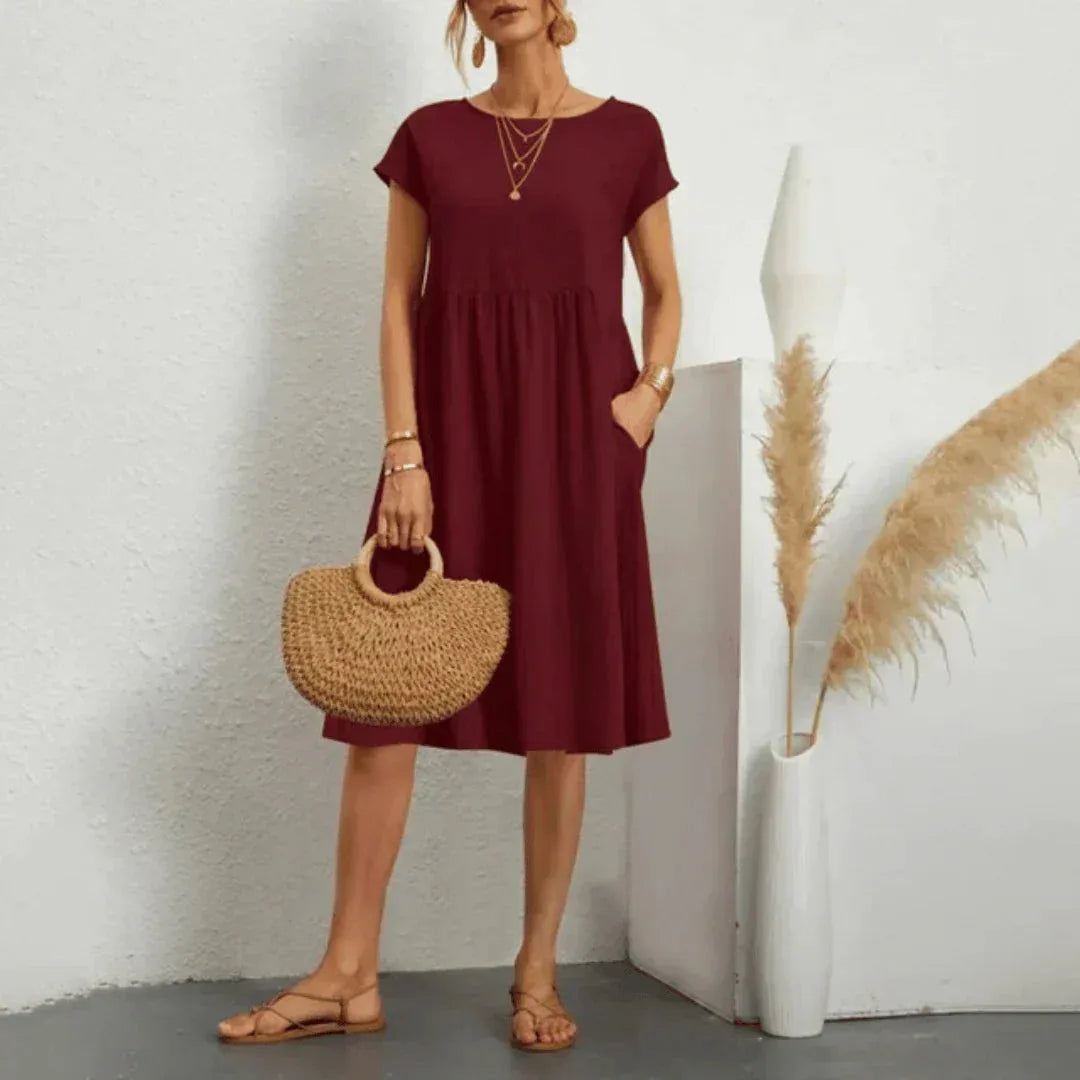 Burgundy cotton-blend swing dress with hand resting in the side pocket, showing the relaxed loose fit