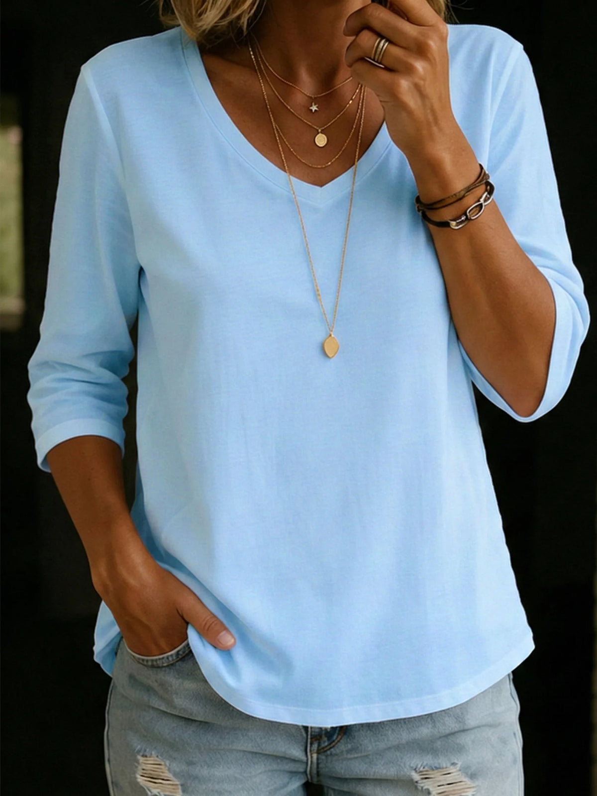 Close-up of pale blue V-neck T-shirt with three-quarter sleeves, styled with a layered gold necklace and ripped denim jeans