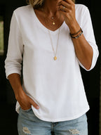 White V-neck cotton T-shirt with three-quarter sleeves, worn tucked loosely with layered gold necklaces and denim shorts