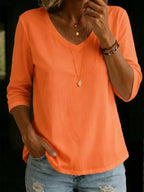 Bright orange V-neck T-shirt with three-quarter sleeves, shown with layered gold jewellery and faded denim jeans