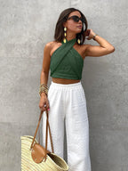 Model wearing the halter top in dark green, styled with gold earrings and white wide-leg pants