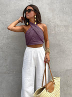 Model wearing the halter top in purple, accessorised with gold bangles and a straw tote bag