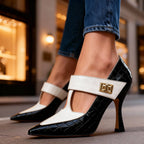 Close-up side view of a black croc-embossed stiletto pump with cream Mary Jane strap and gold buckle, worn with jeans