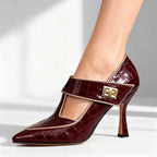 Studio close-up of burgundy croc-textured pump with tan trim, T-strap and gold buckle on plain grey backdrop