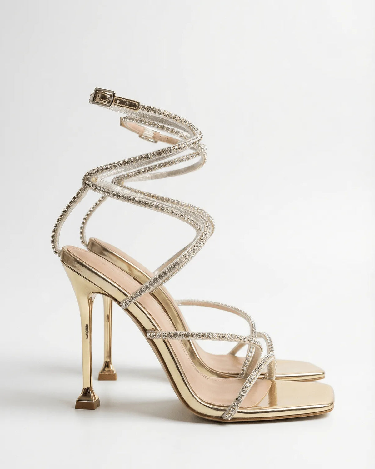 Side view of a gold strappy stiletto sandal with crystal-embellished straps spiralling up the ankle and a square open toe.