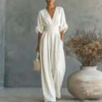 Woman wearing a white V-neck wide-leg jumpsuit with wrap bodice, cinched waistband and 3/4 cuffed sleeves