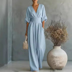Light blue V-neck jumpsuit with pleated waist panel, flowing wide-leg trousers and side pockets, front view