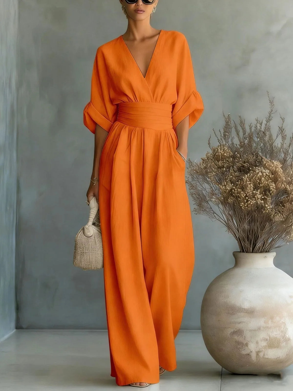 Orange wide-leg jumpsuit with wrap V-neckline, ruched waist belt and cuffed sleeves, worn with strappy sandals